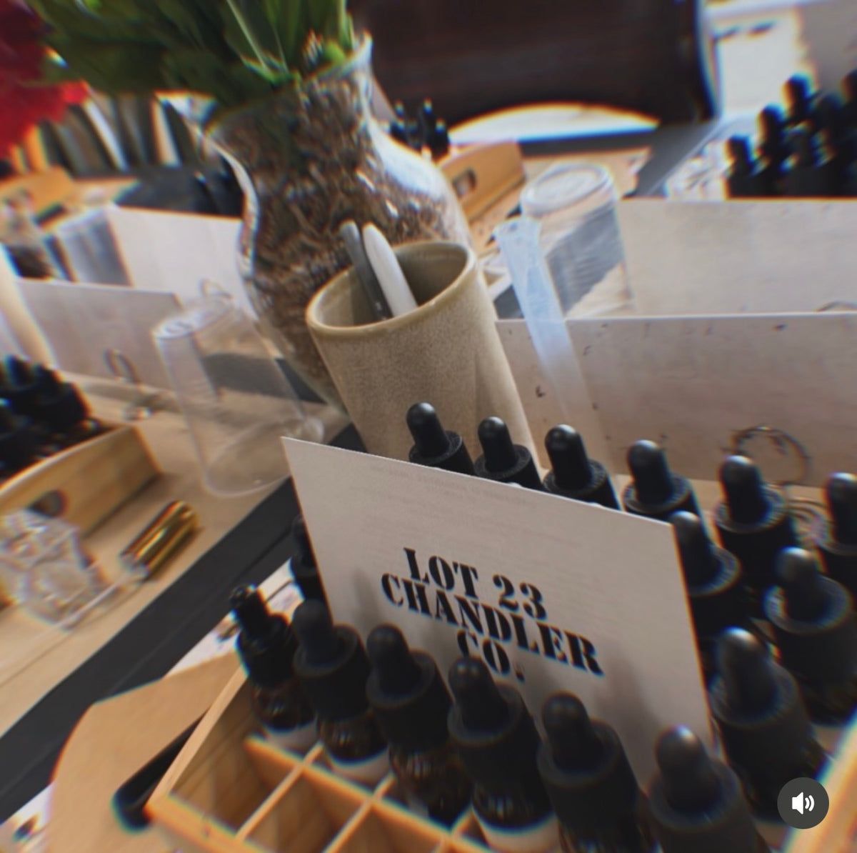 A close-up of a display of small amber glass dropper bottles arranged in a wooden tray, with a sign reading 'LOT 23 CHANDLER CO.' in the center.