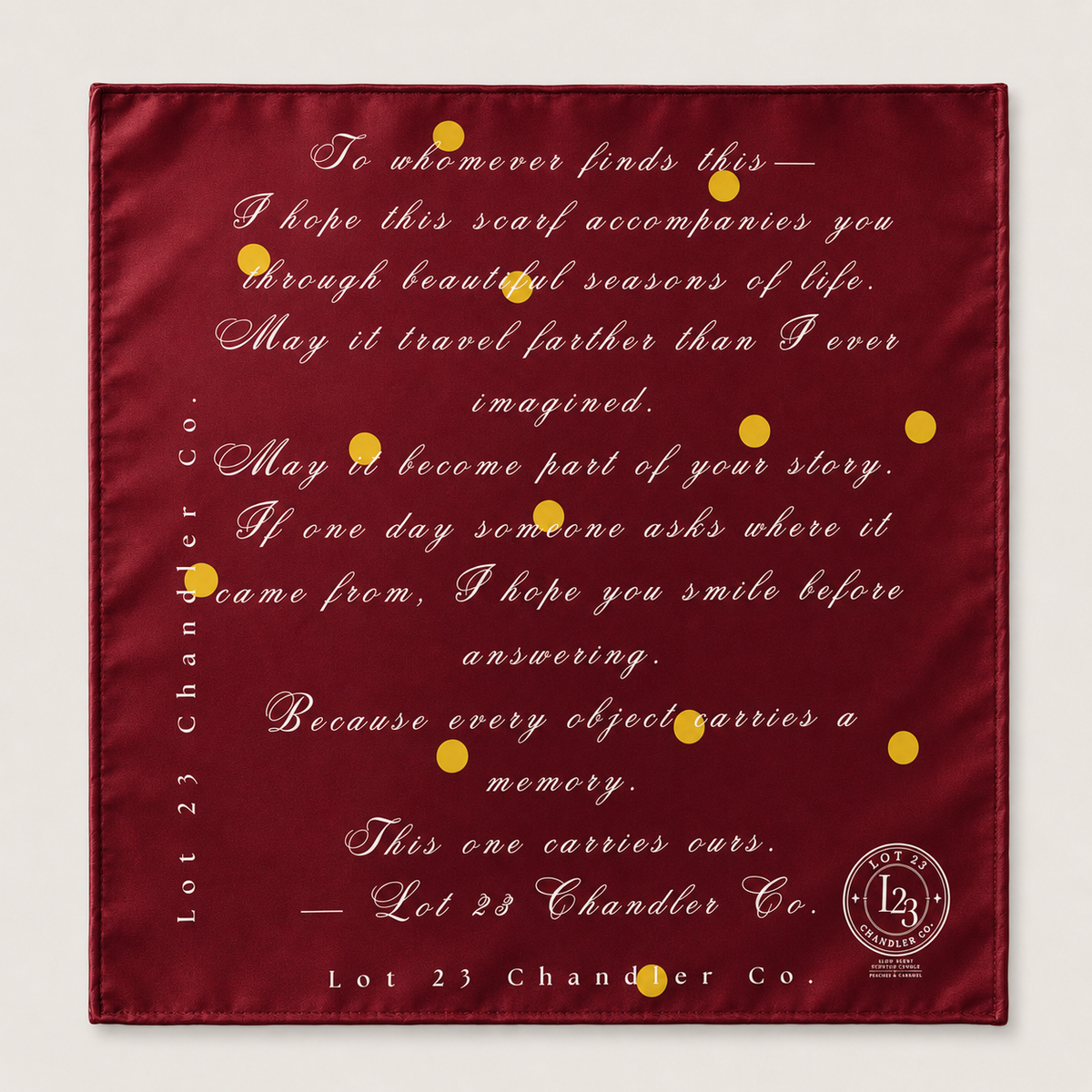 A square burgundy satin scarf with elegant gold cursive text and small gold dots, featuring a quote from Lot 23 Chandler Co. and their brand logo in the bottom right corner.